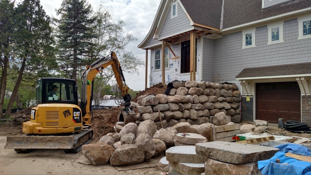 An excavator operator at Landscapes Unlimited hand selects and carefully places boulders for this retaining wall to allow for a walkout garage.